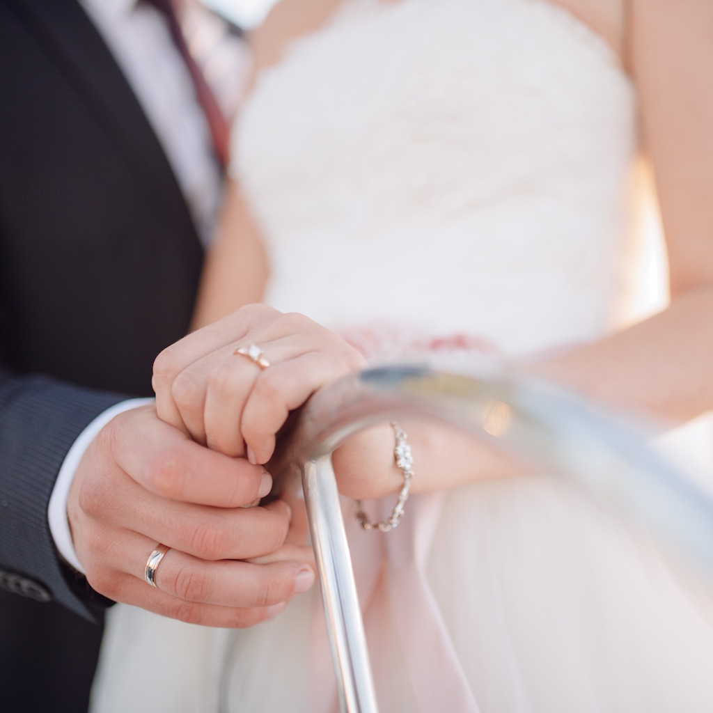 Hochzeitspaar hält sich am Steuer eines Schiffs fest.