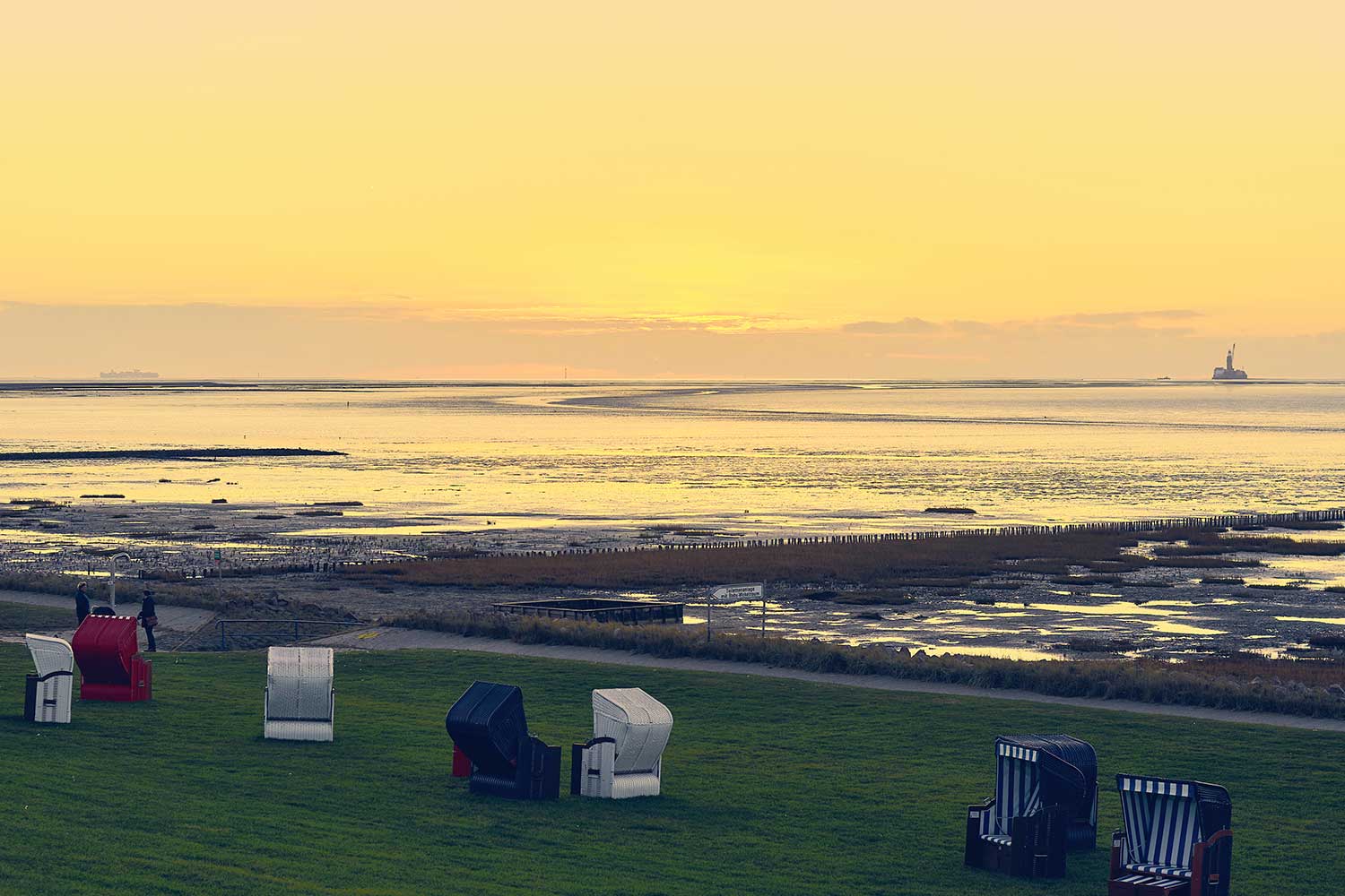Blick vom Deich in Freidrichskoog auf über das Watt auf die Ölplattform Mittelplate bei Sonnenuntergang.